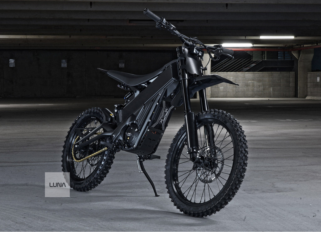 Black electric dirt bike in a dimly lit indoor setting with 'LUNA' branding.