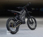 Black electric dirt bike on a wooden floor with a dark background